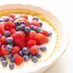 A no-bake lemon pie filled with a creamy base and topped with fresh strawberries, raspberries, and blueberries is displayed in a white ceramic dish.