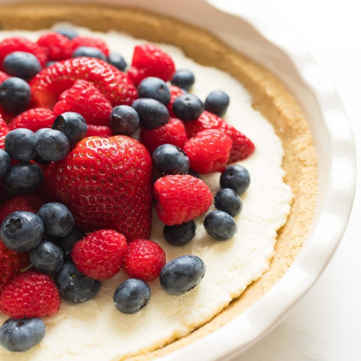A no bake lemon pie in a white pie dish, topped with fresh berries