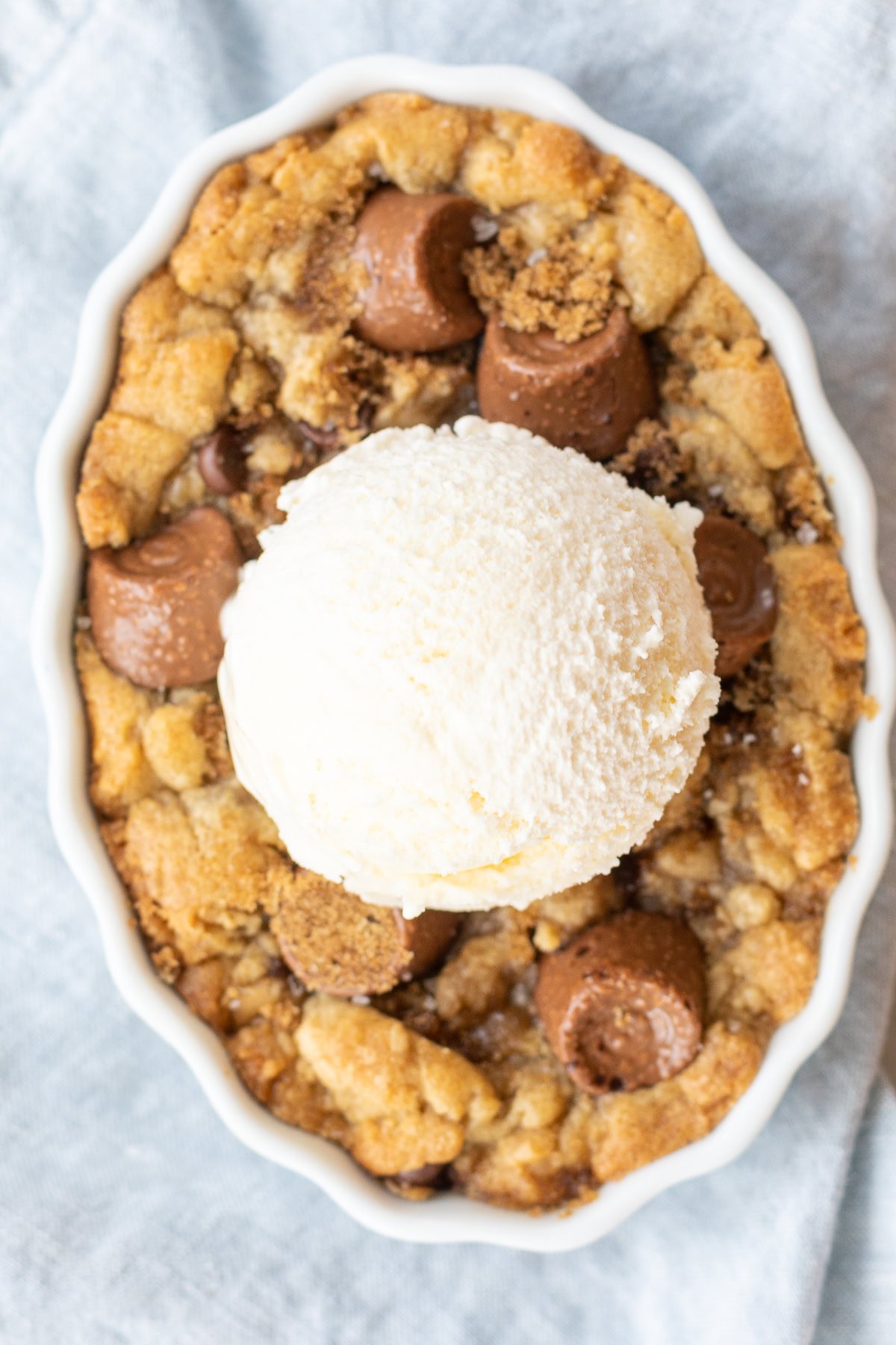 A chocolate chip cobbler topped with a scoop of vanilla ice cream, featuring a crumbly, golden-brown base with pieces of chocolate.