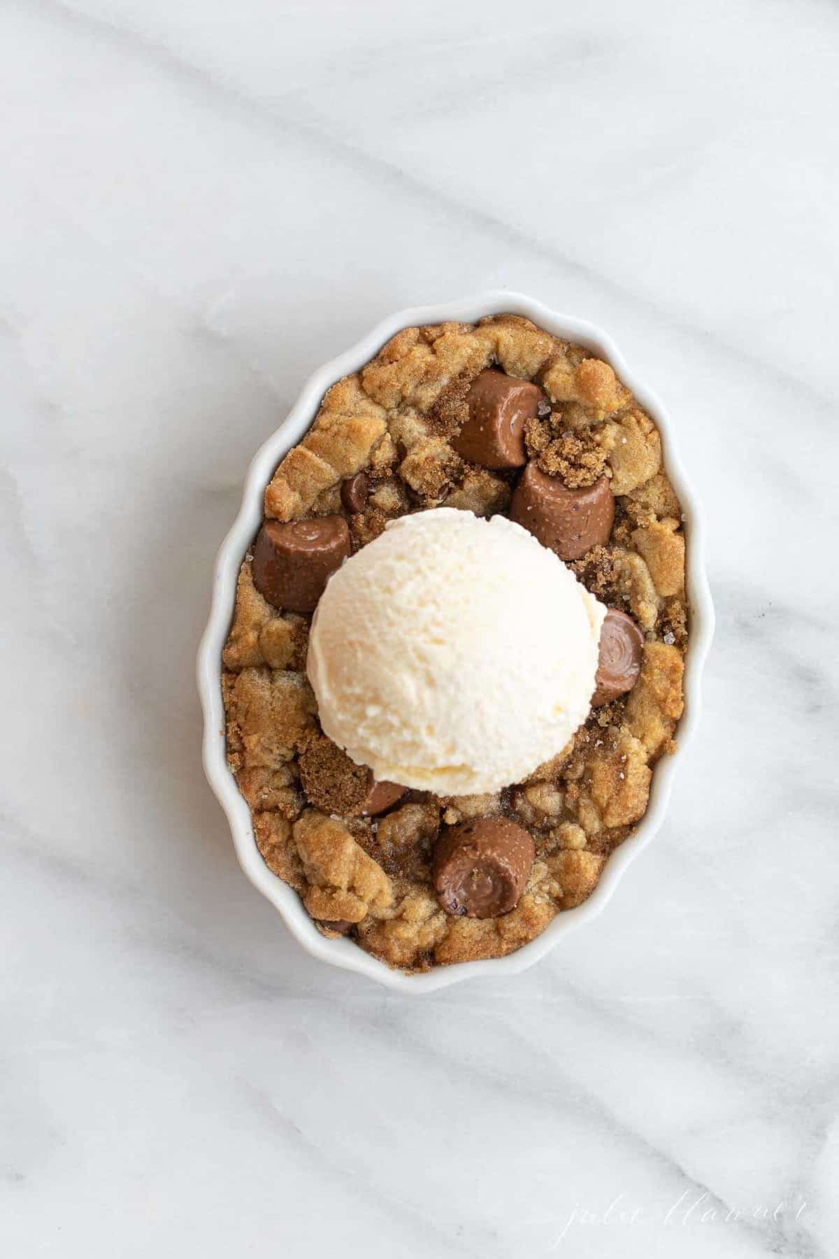 Salted caramel chocolate chip cobbler in a white dish topped with vanilla ice cream. 