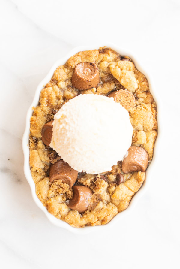 A chocolate chip cobbler topped with a scoop of vanilla ice cream, featuring a crumbly, golden-brown base with pieces of chocolate.