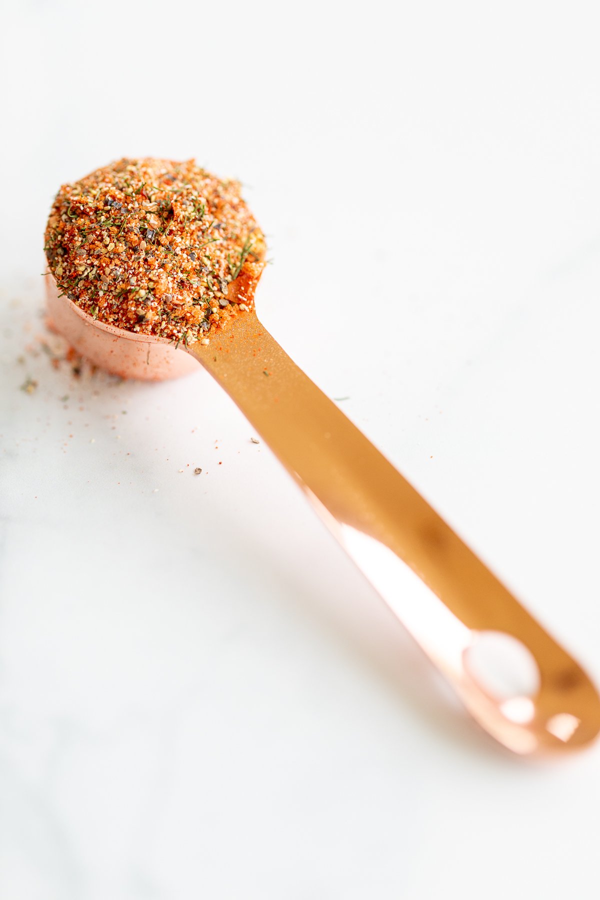 A spoon filled with the best steak seasoning on a marble countertop.