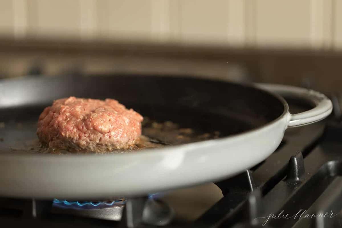 A burger being cooked in a cast iron pan. 