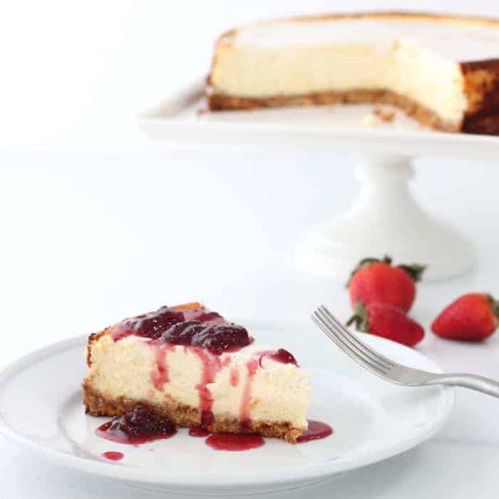 A white plate with a slice of cheesecake with strawberry topping.
