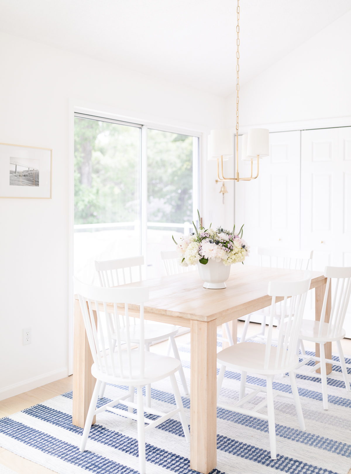 A white kitchen with a teak dining table and a blue and white striped rug