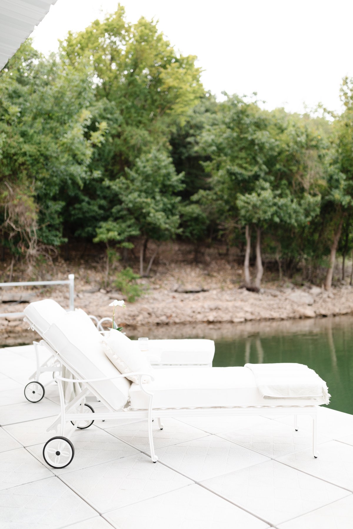 White metal chaise lounges on a dock, with trees in the background