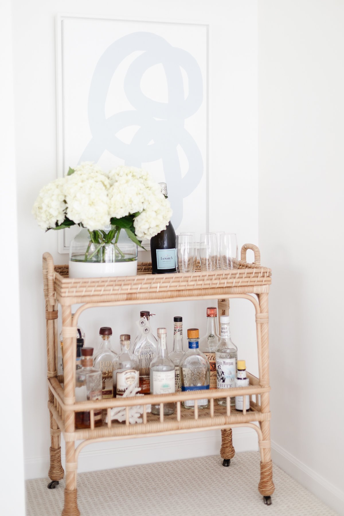 A rattan bar cart with blue and white modern art above it.