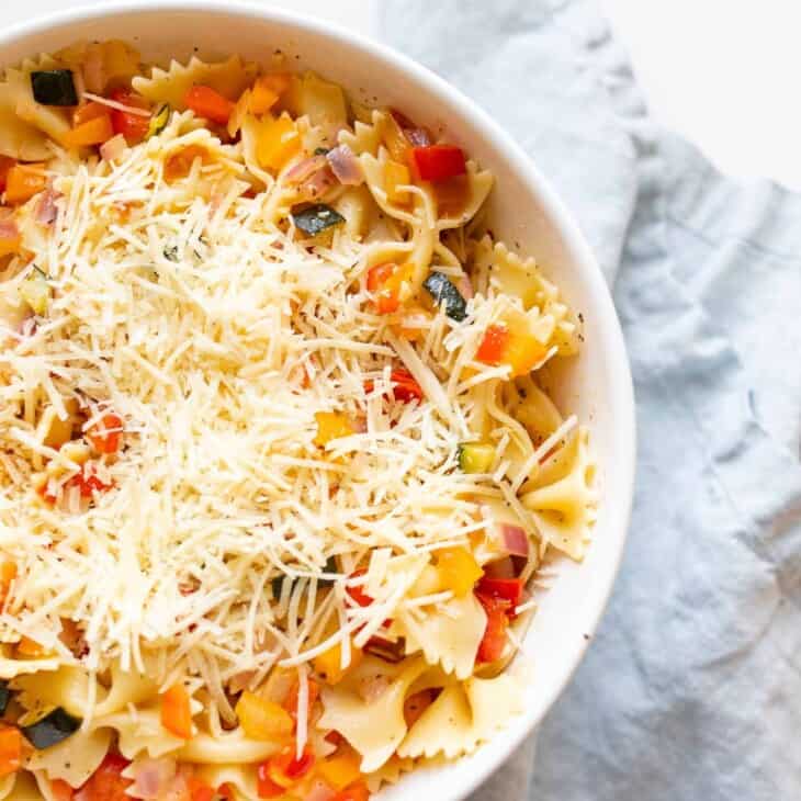 A white bowl filled with a fresh vegetarian pasta salad topped with Parmesan cheese.