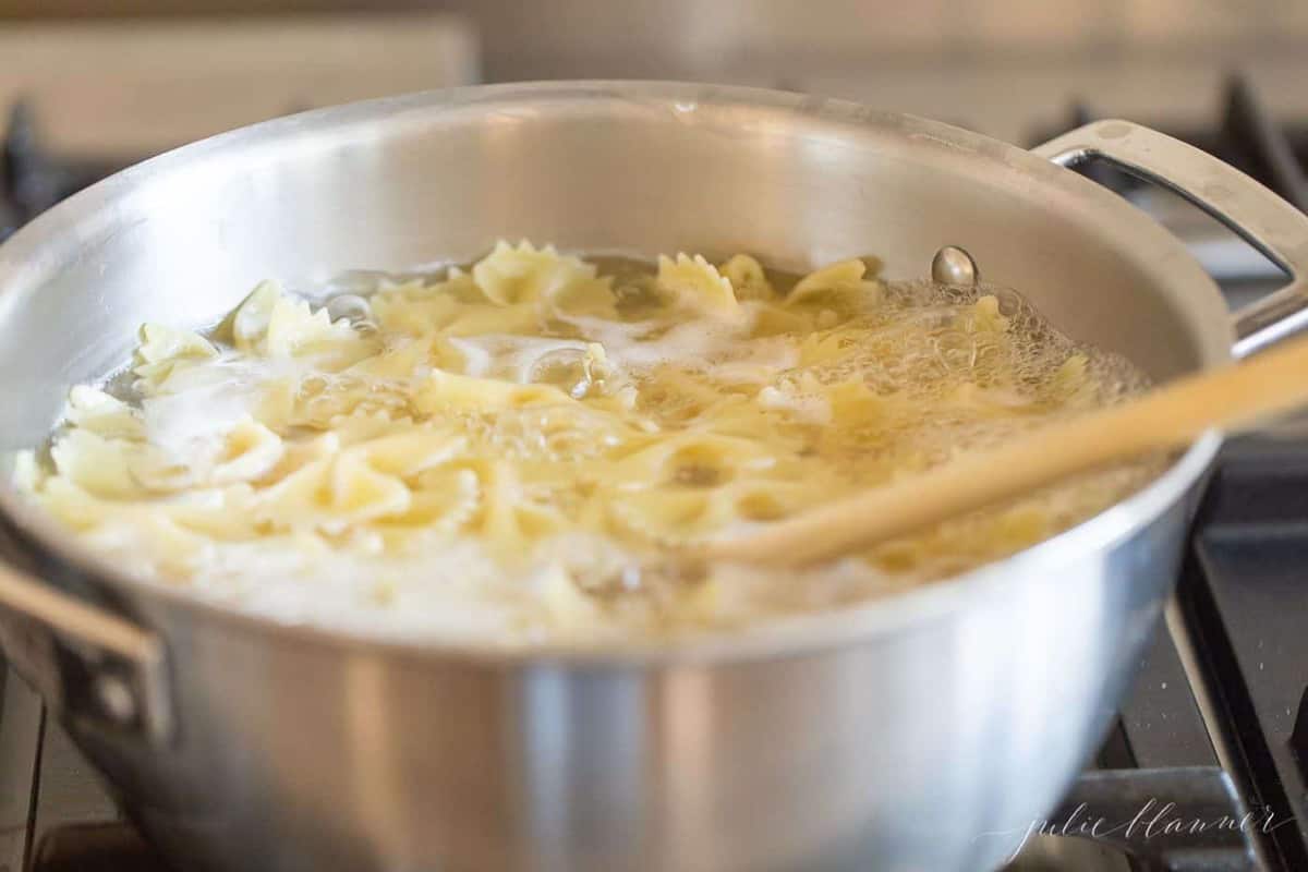 A silver stockpot filled with bowtie pasta as it cooks.