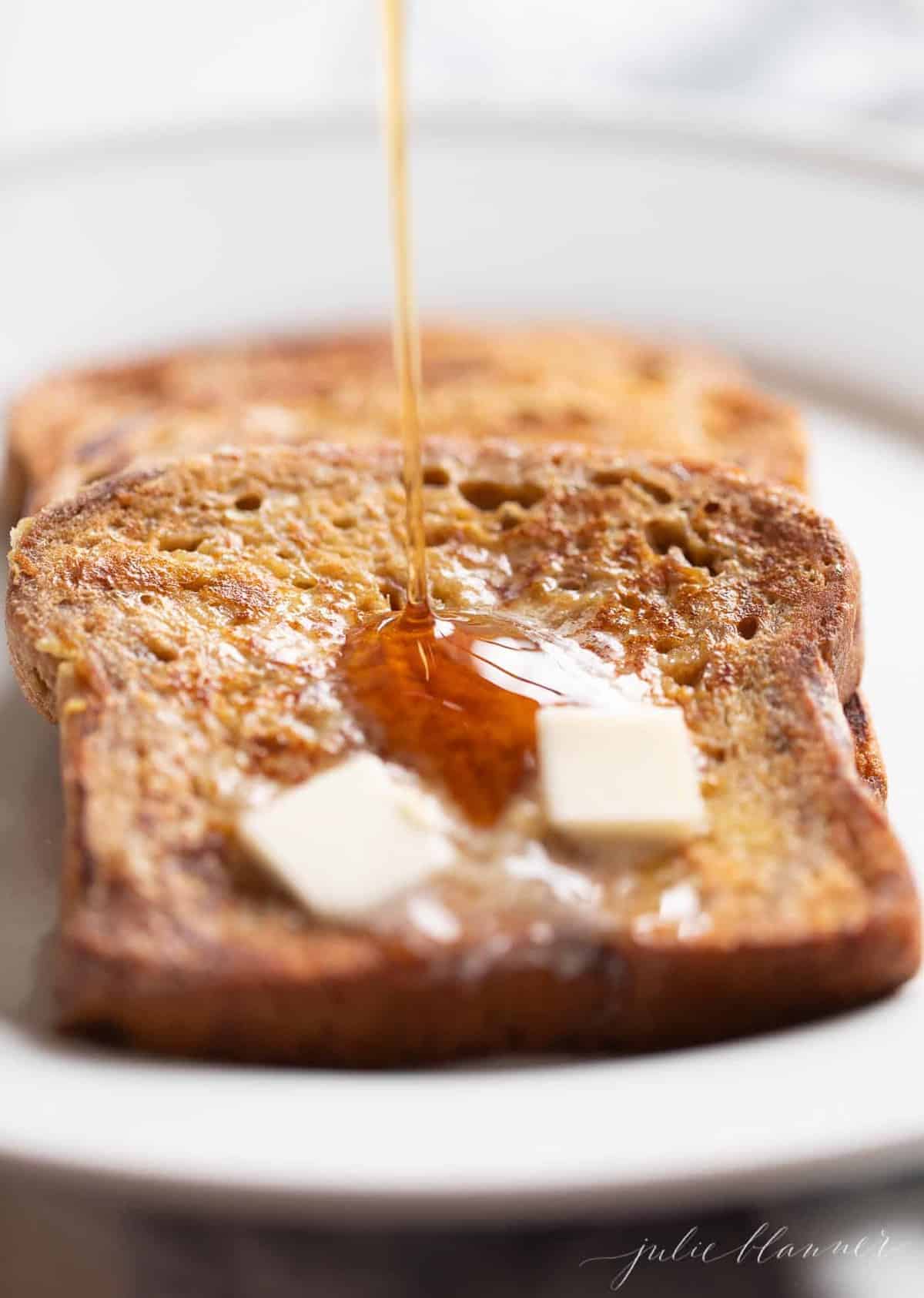 Close up shot of apple fritter french bread, pats of butter on top and syrup being poured.