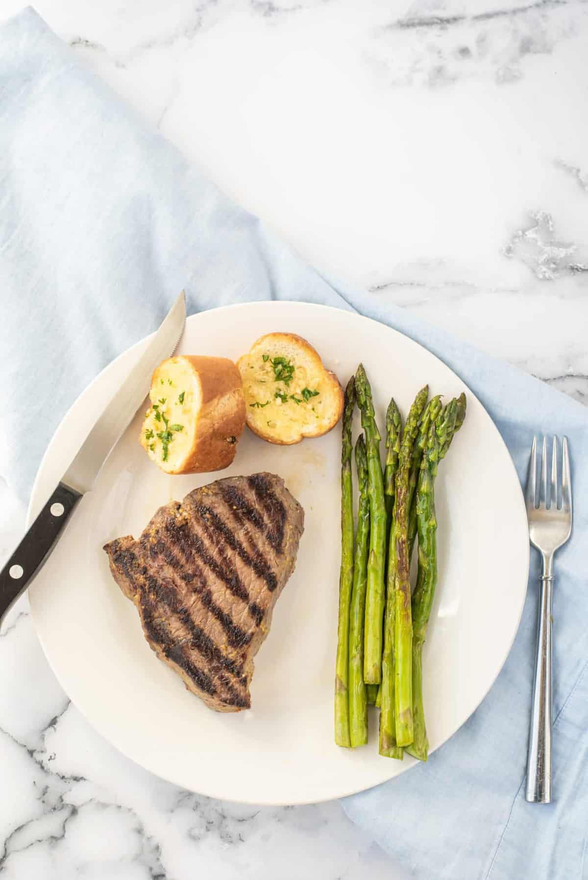 A grilled steak with a side of asparagus on a white plate.