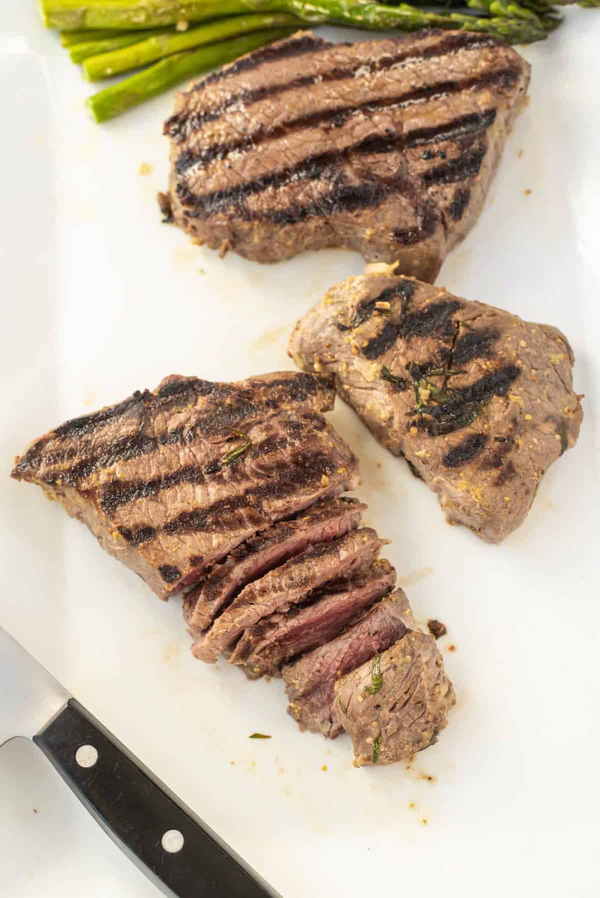 A white plate with marinated steak, first one sliced.