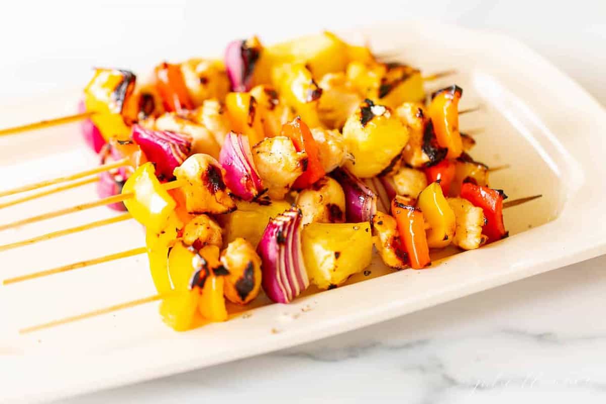 Colorful chicken kabobs on a cream platter.