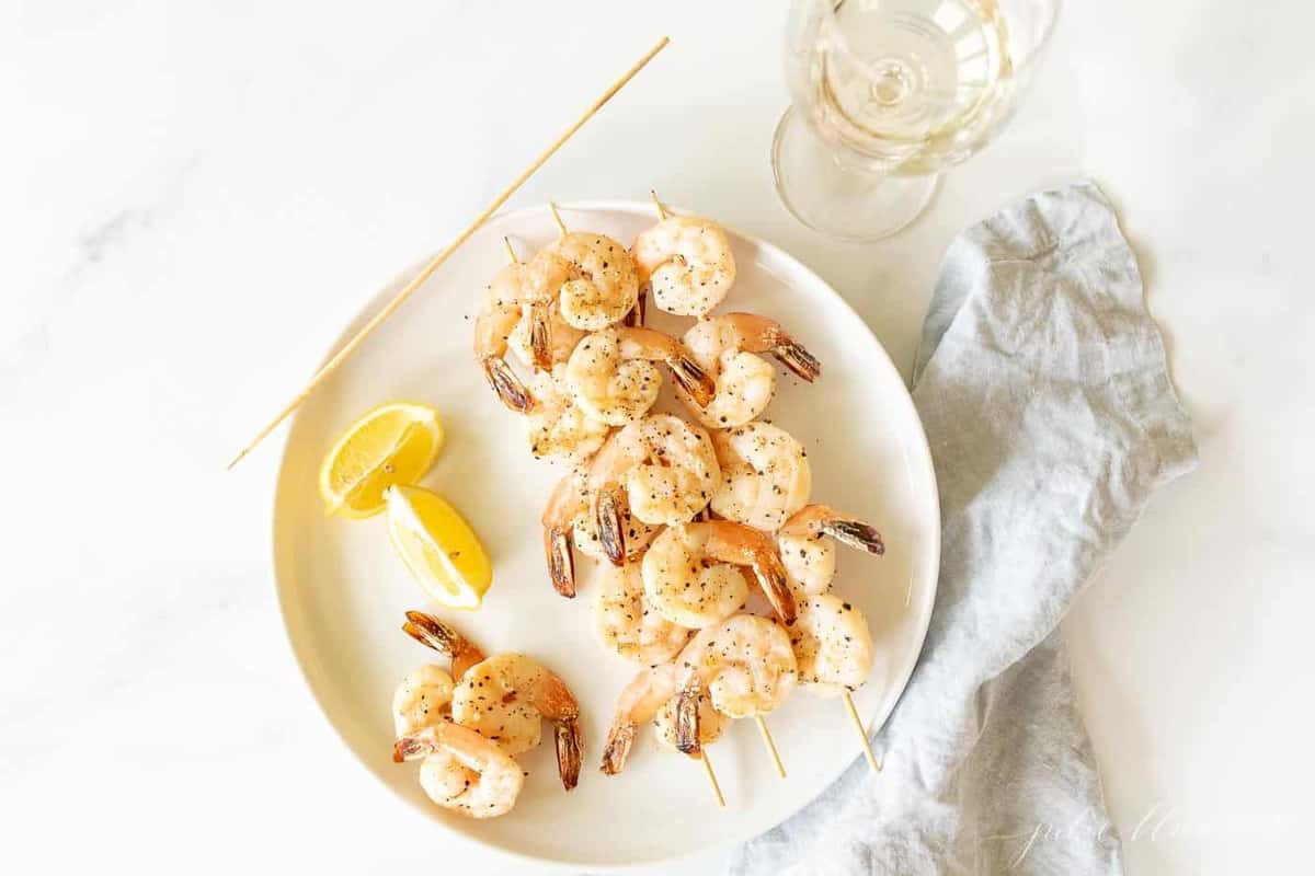 A white plate with skewers of lemon garlic shrimp kabobs.