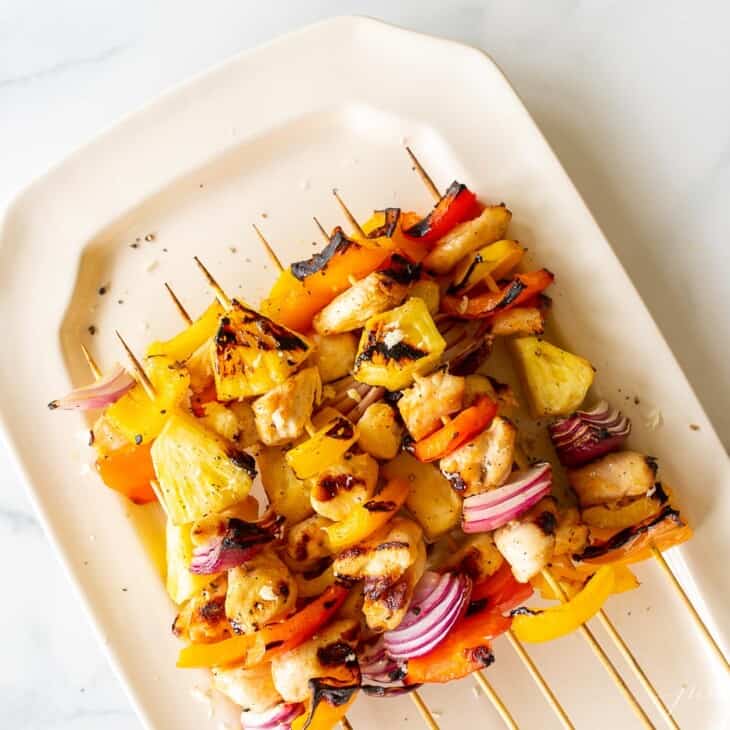 A white platter full of chicken kabobs on a marble surface.