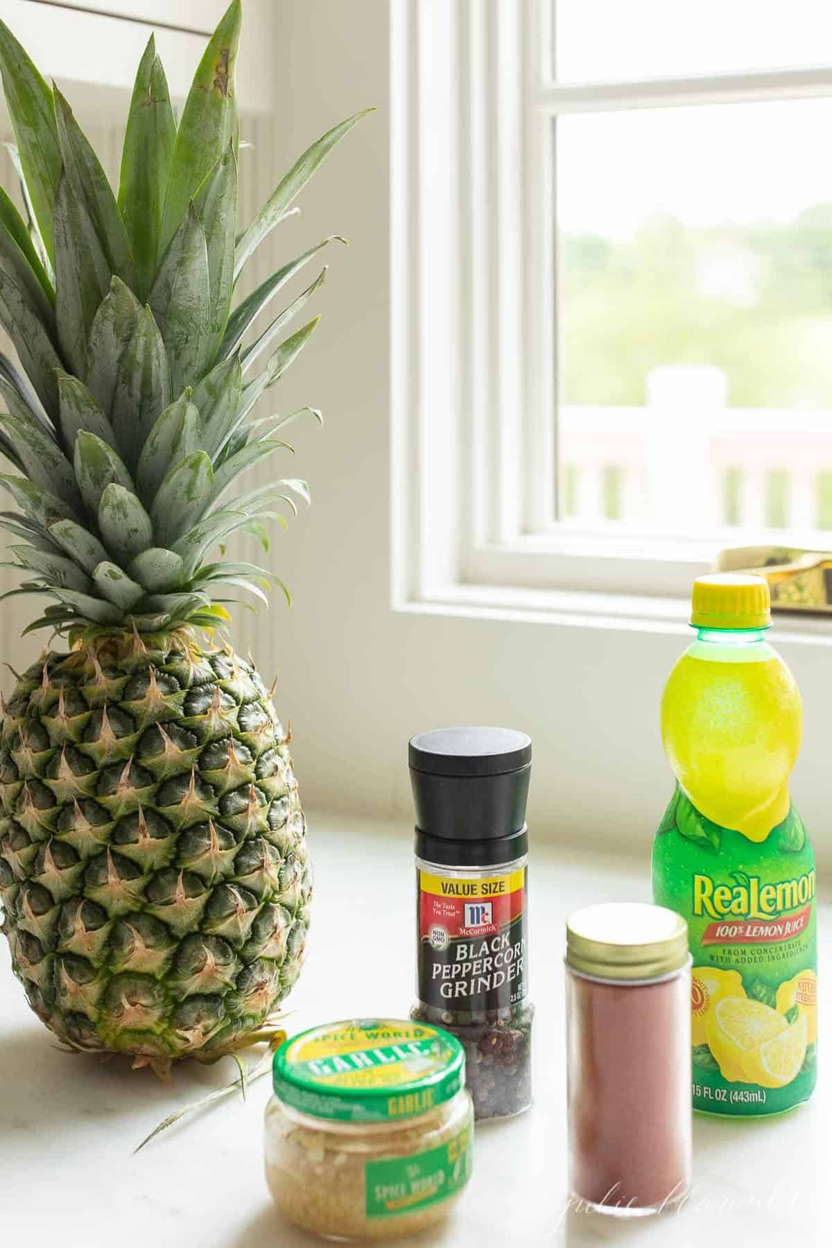 Pineapple surrounded with various spices in front of a window.