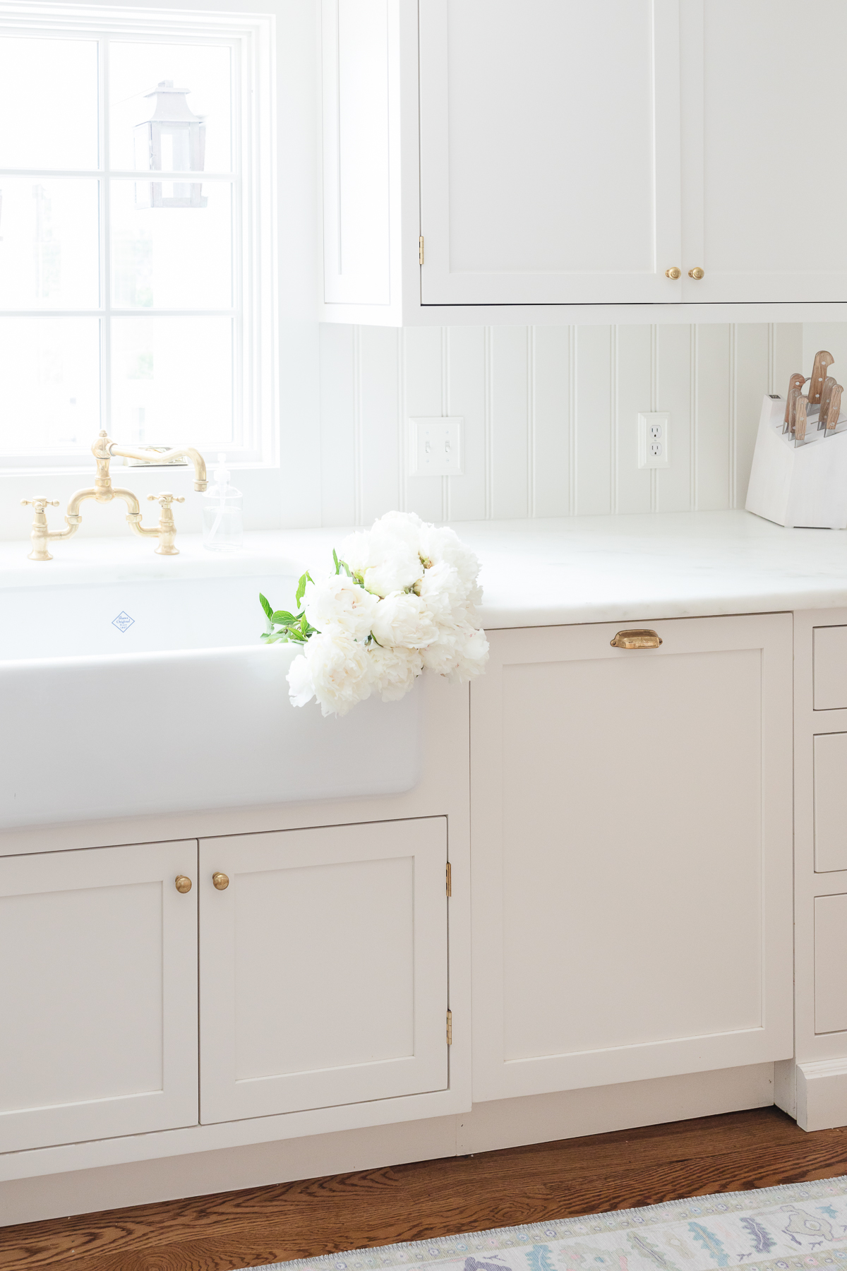 A cream kitchen with brass hardware, a farm sink and Danby marble countertops.