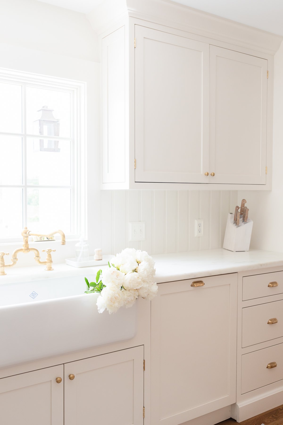 A cream kitchen with brass hardware, a farm sink and Danby marble countertops.