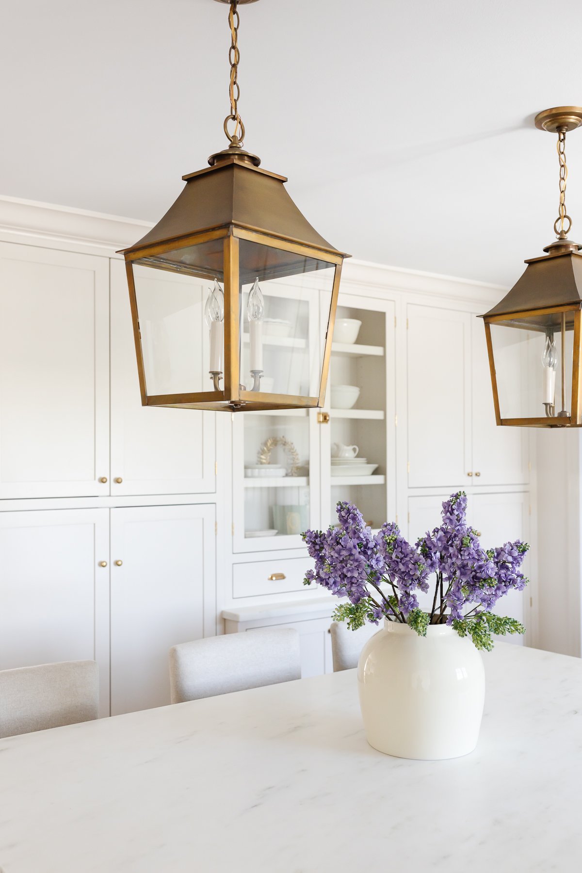 A cream kitchen with brass lantern pendants, a wood island and Danby marble countertops.