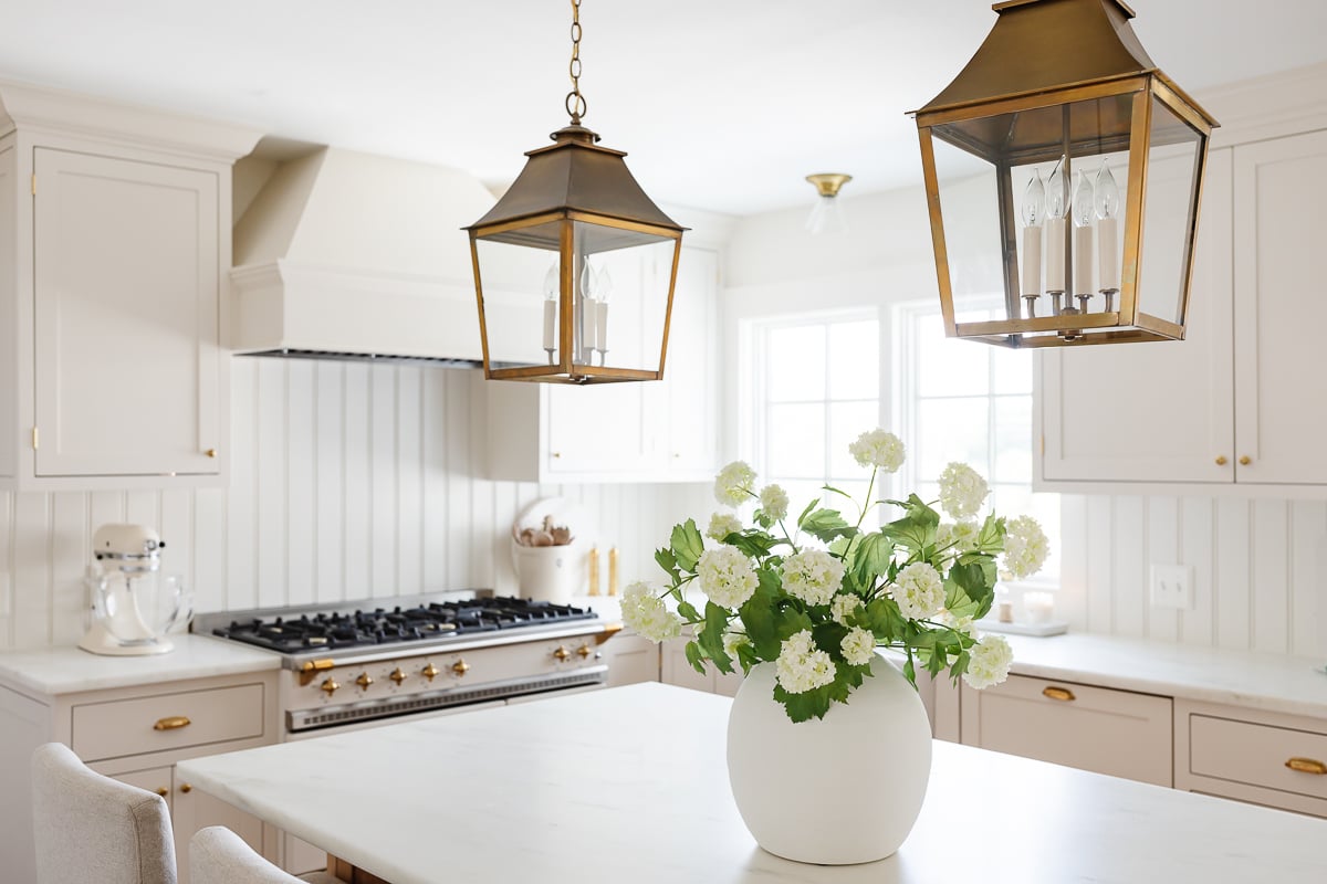 A cream kitchen with brass lantern pendants, a wood island and Danby marble countertops.