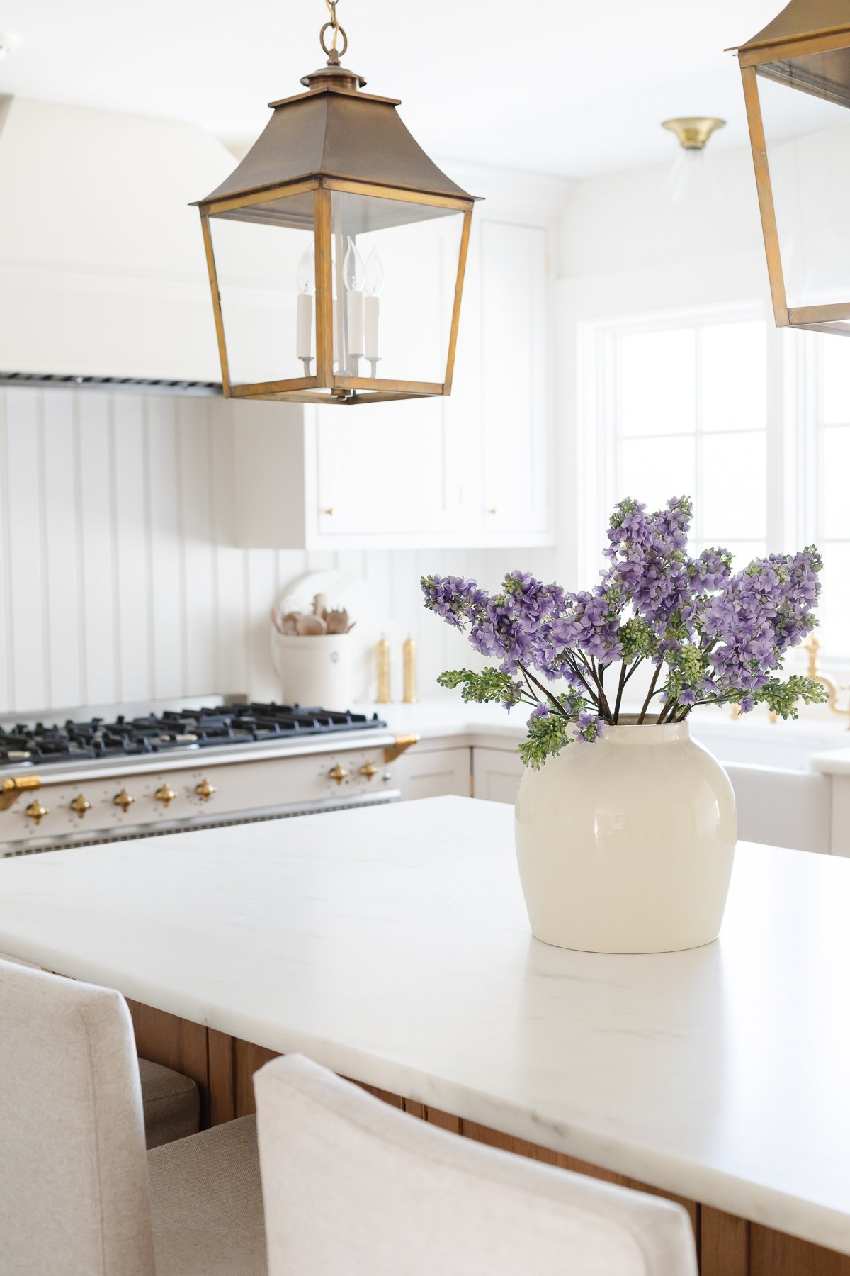 A cream kitchen with brass hardware, a farm sink and Danby marble countertops. 