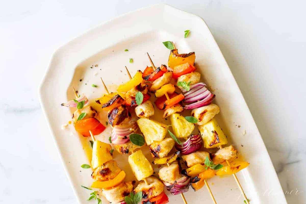 Colorful chicken kabobs on a cream platter.