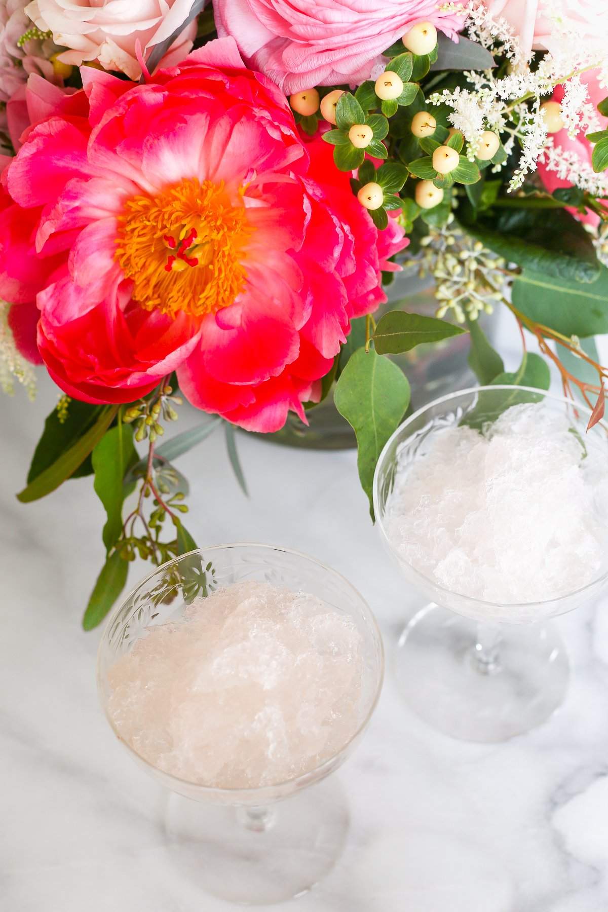 Two glasses with ice in them next to a bouquet of flowers, perfect for enjoying a refreshing frosé.