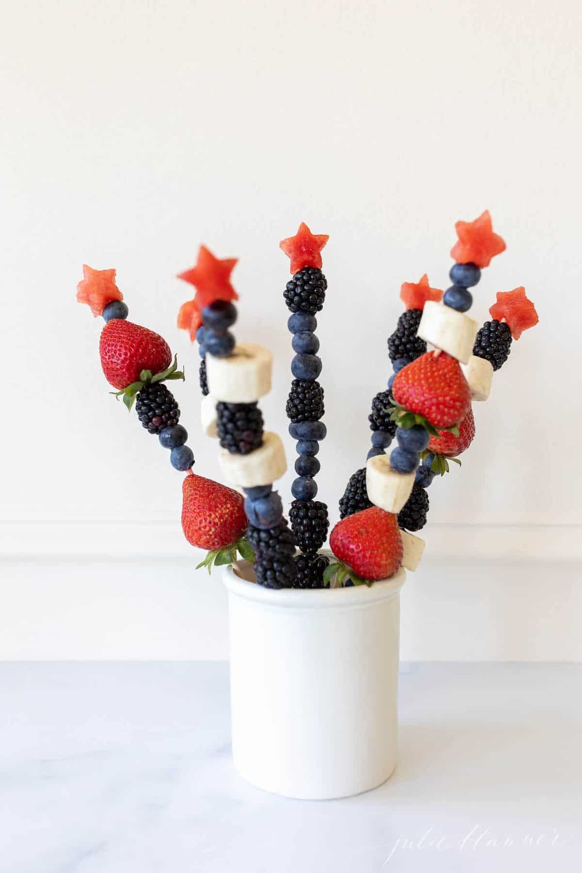 Marble surface with a white canister filled with fresh fruit skewers.