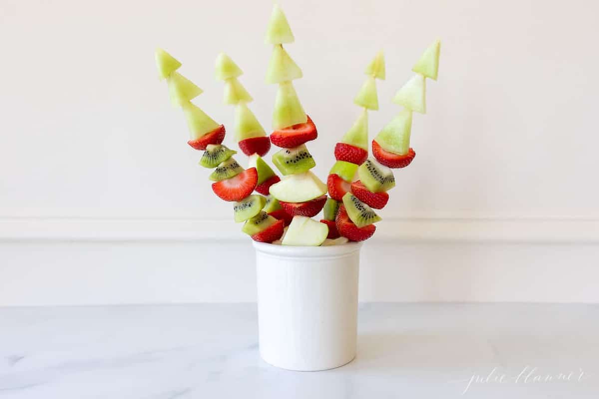 Marble surface with a white canister filled with fresh fruit skewers.