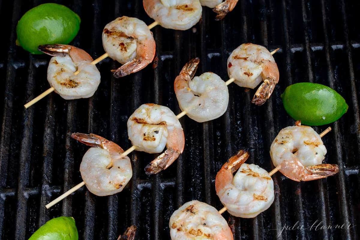 Shrimp skewers on the grill with sliced limes on the side.