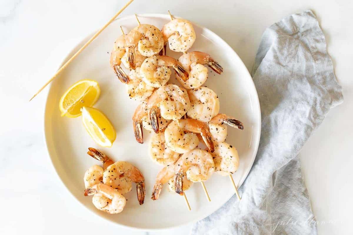 A white plate with skewers of lemon garlic shrimp kabobs.