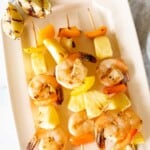 A white platter filled with pineapple shrimp skewers.