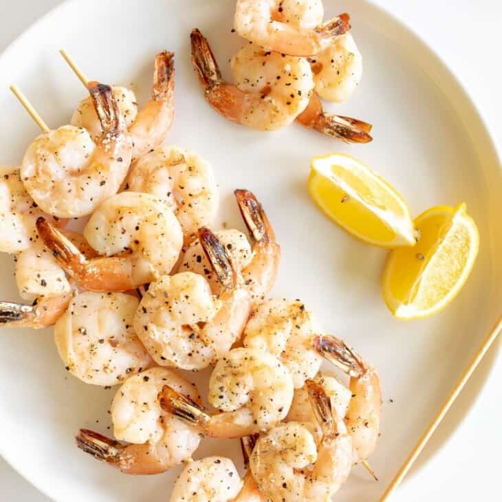 A white plate with skewers of lemon garlic shrimp kabobs.
