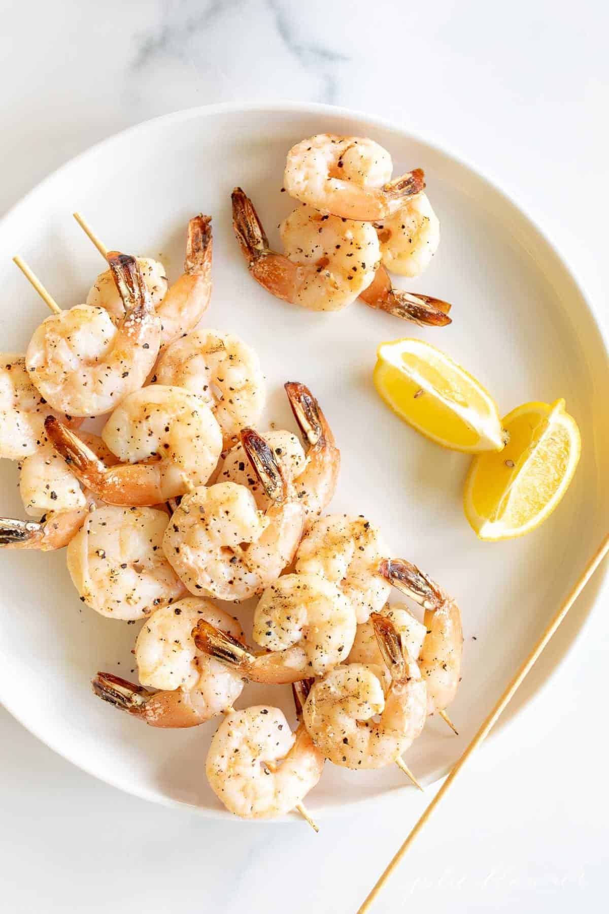 A white plate with skewers of lemon garlic shrimp kabobs.