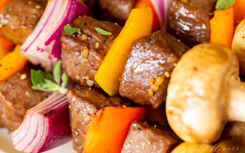 A close up image of steak kabobs on a white platter.