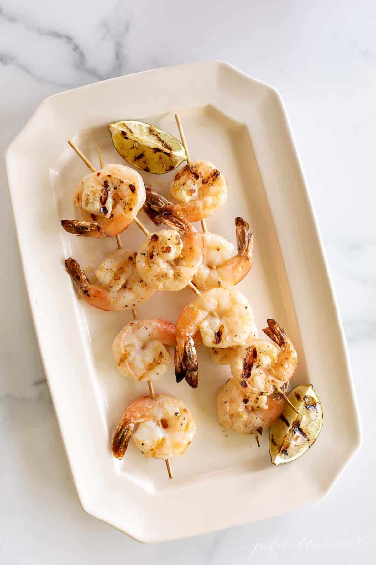 A white platter filled with grilled shrimp skewers.