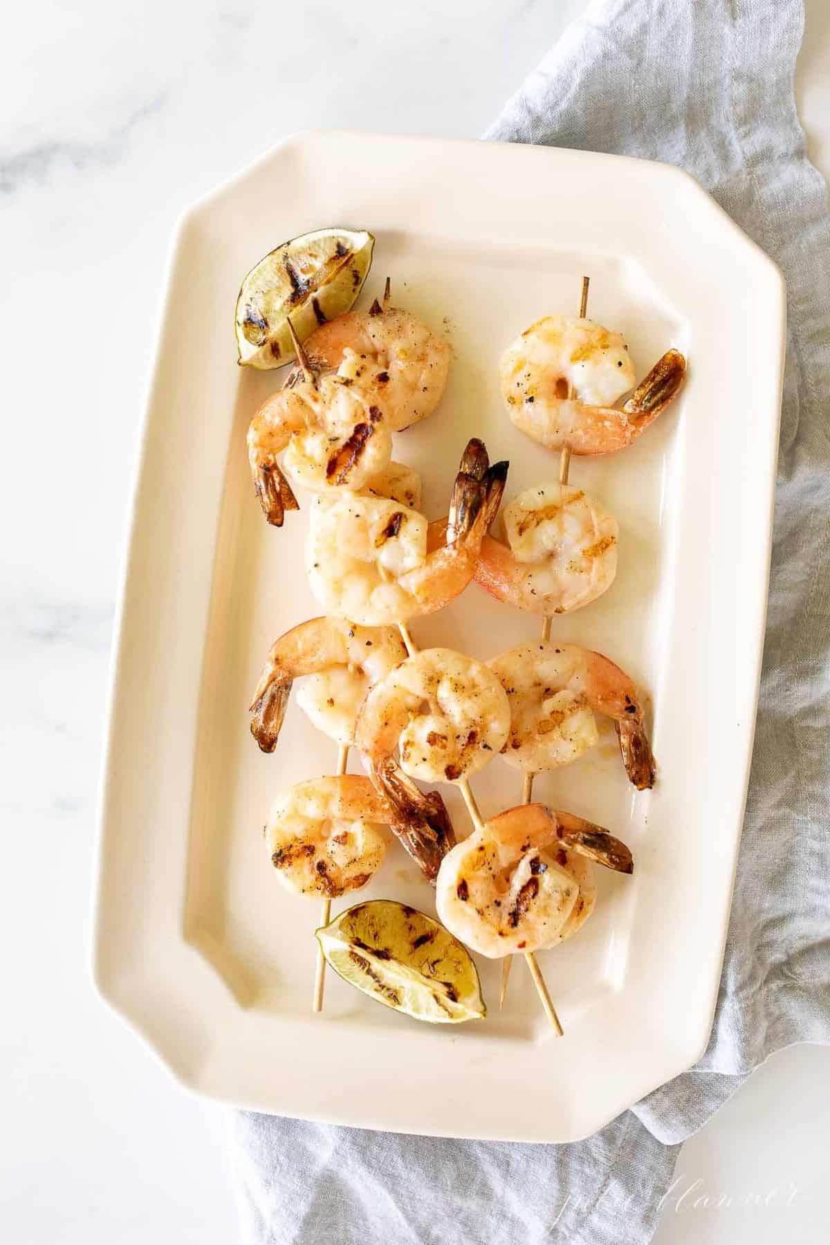 A white platter filled with grilled shrimp skewers.