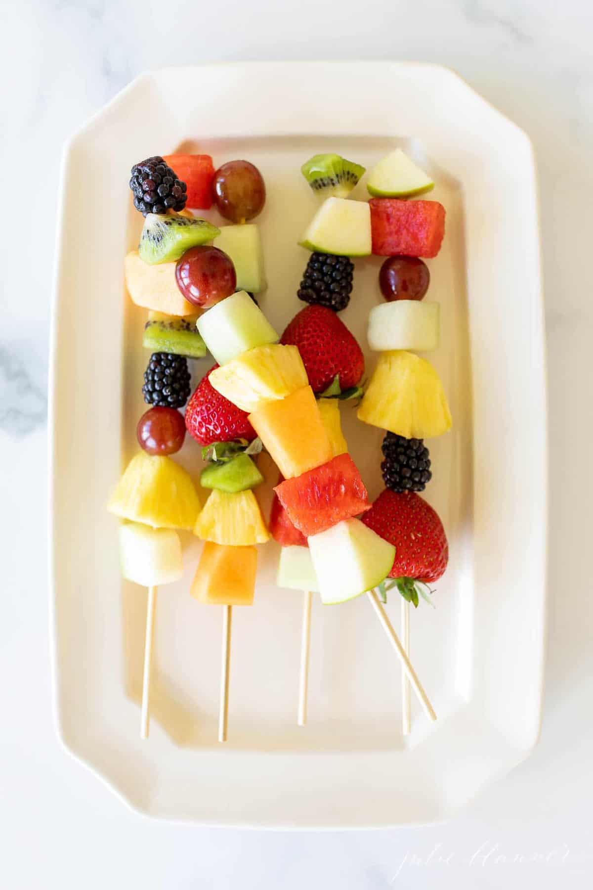 Colorful fruit skewers on a white platter.