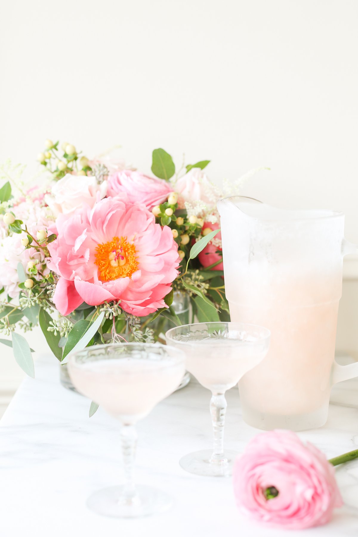 A pitcher of pink frosé sangria on a table next to a bouquet of pink flowers.