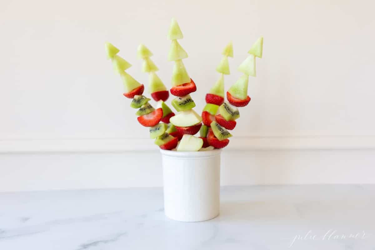 Marble surface with a white canister filled with fresh fruit skewers.