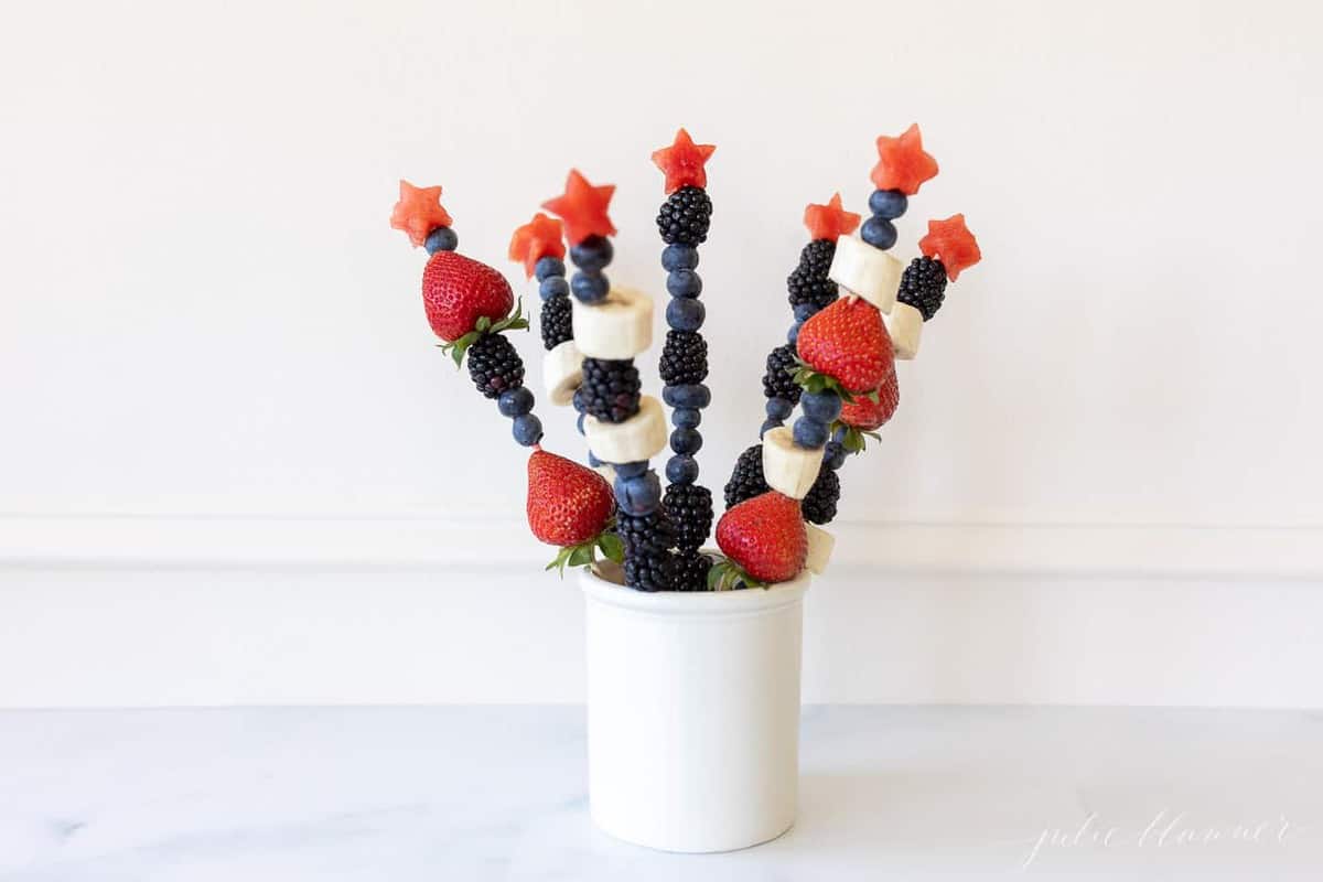 Marble surface with a white canister filled with fresh fruit skewers.