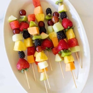 Colorful fruit skewers on a white oval platter.