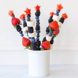 red white and blue fruit skewers displayed in a white ceramic container.