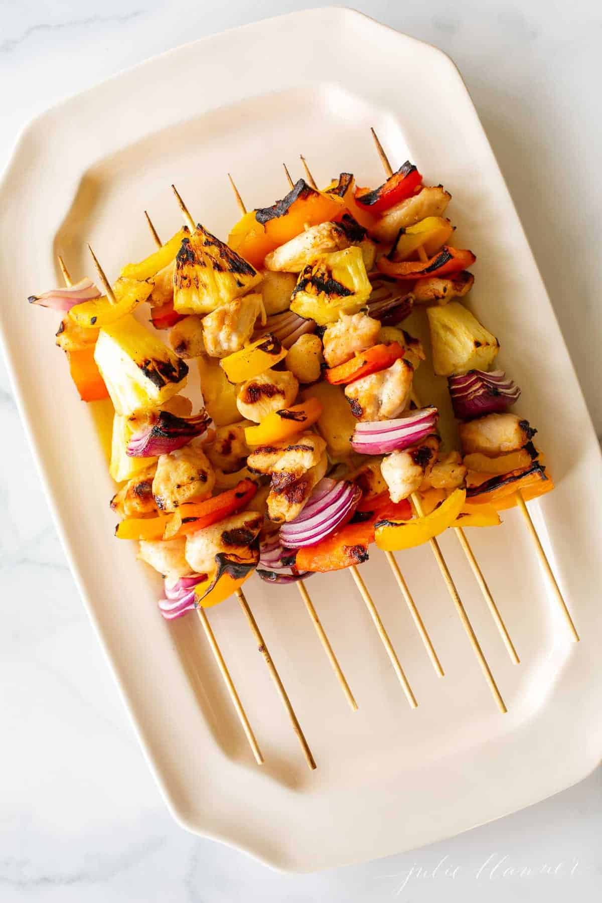 Colorful chicken kabobs on a cream platter.