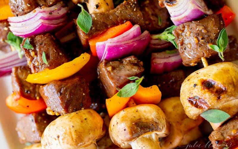 A close up image of steak kabobs on a white platter.