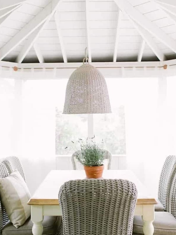 Wicker seating at a dining table on a screened in porch, a pot of English lavender as the centerpiece.