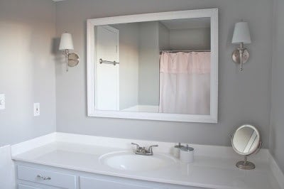 Bathroom with a white cabinet, large white framed mirror and gray walls.