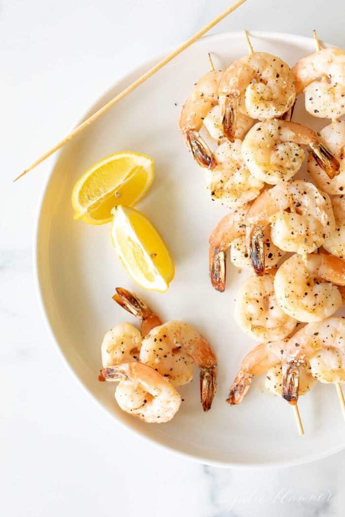 A white plate with skewers of lemon garlic shrimp kabobs.