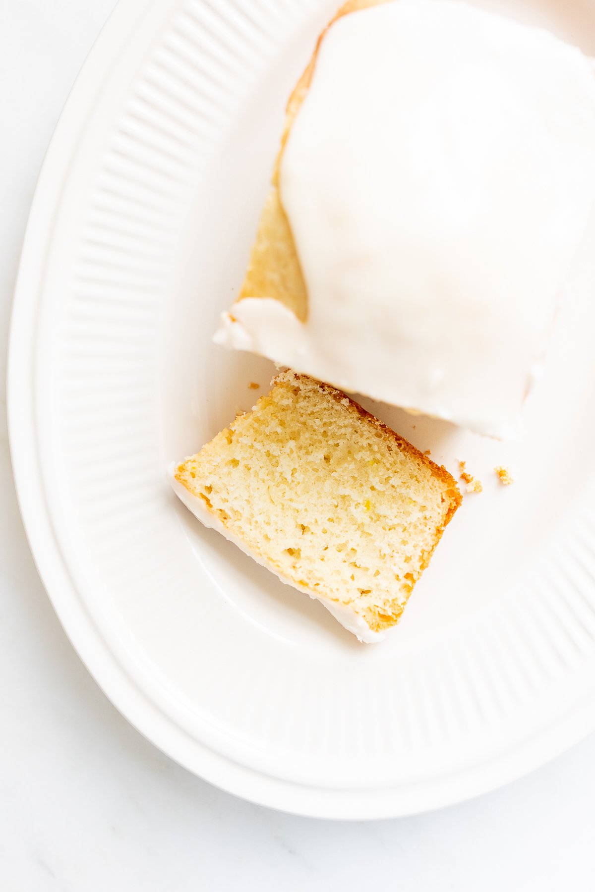 A sliced lemon cake with lemon glaze on a white oval plate.