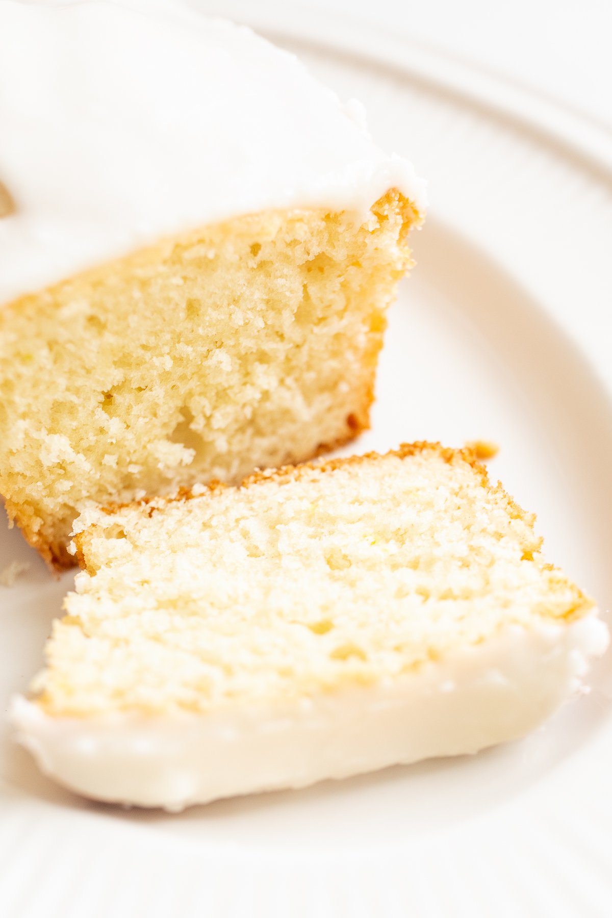 A slice of lemon breadwith lemon glaze icing on a plate, showing a moist crumb with a piece cut off.
